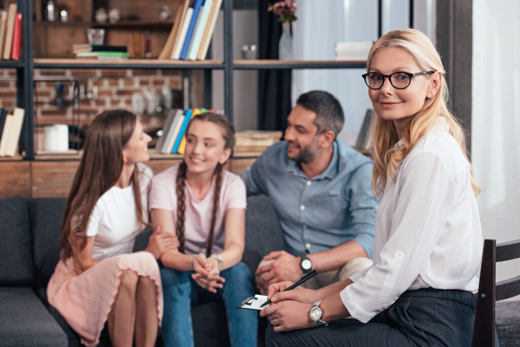 smiling female psychiatrist looking at camera while happy family at a family therapy