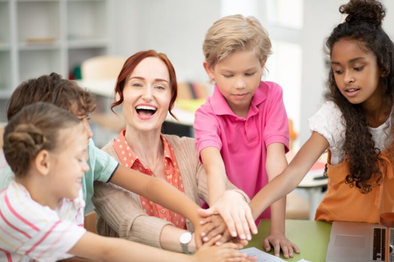 An adult and children stacking their hands together during a group activity.