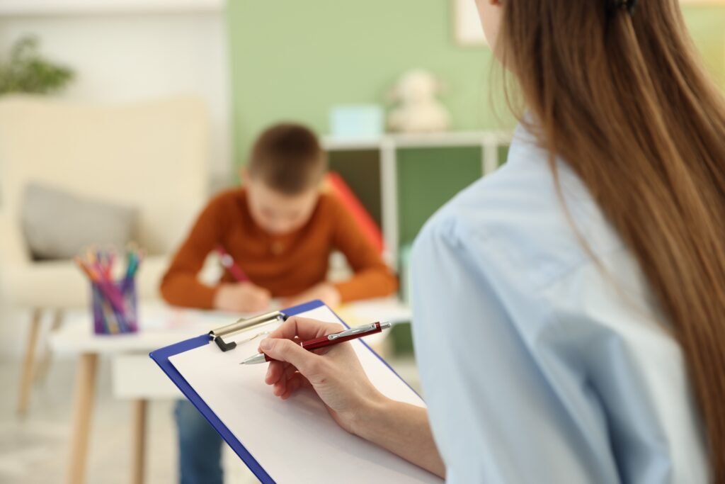 Woman taking notes while a child works at a table.