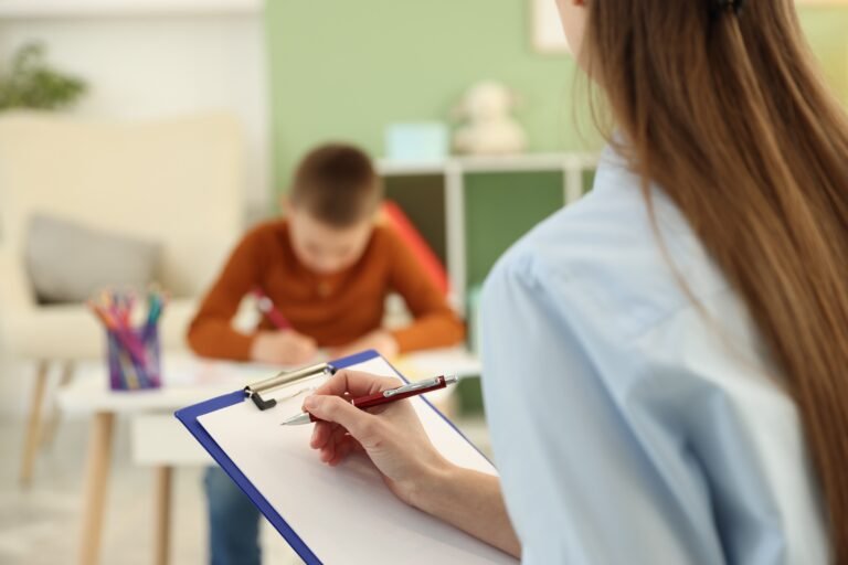 Woman taking notes while a child works at a table.