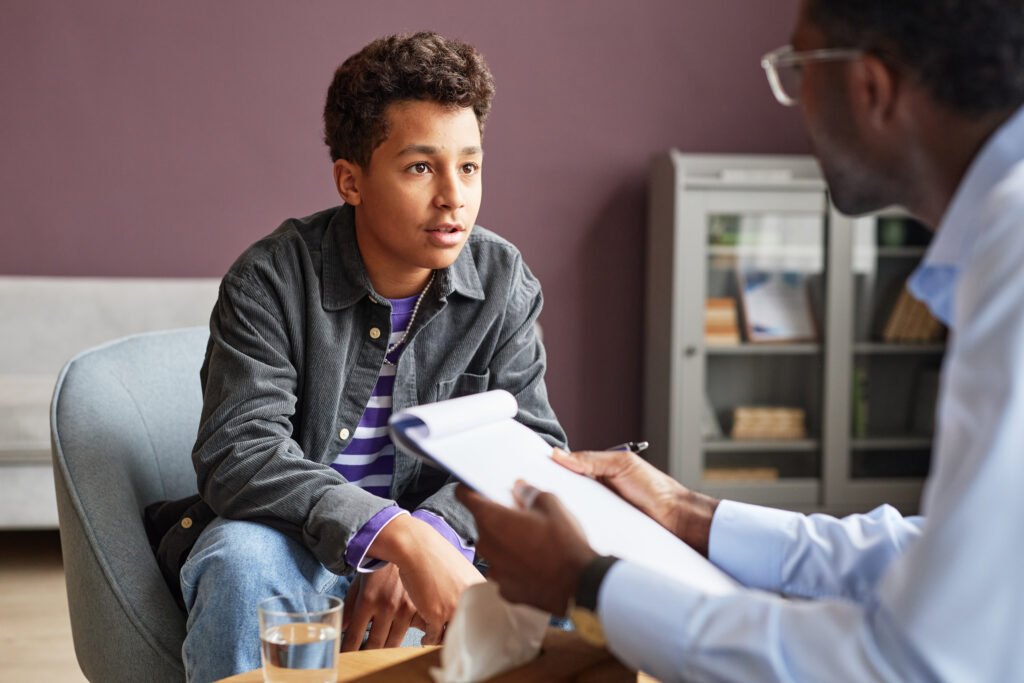 Teen boy talking with an adult who is holding a notepad.