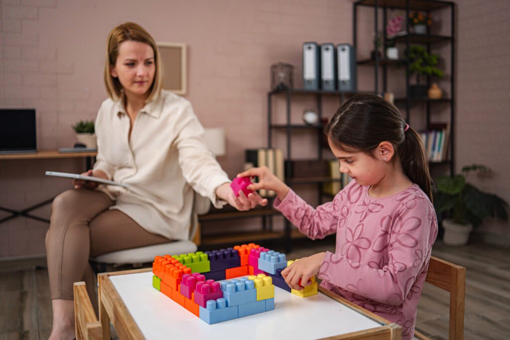 Girl arranging colourful building blocks with an adult nearby.